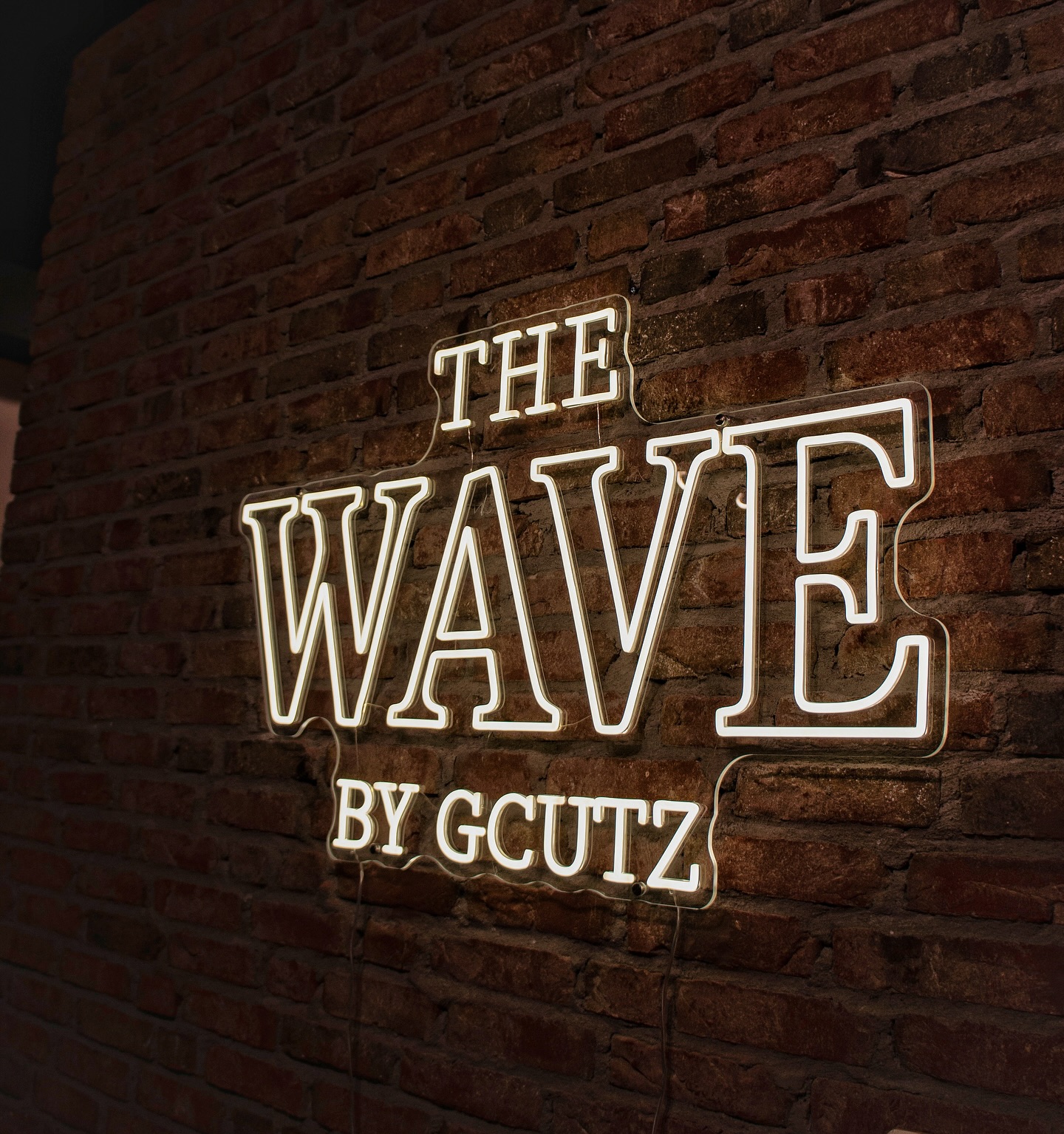 Het neonbord The Wave by Gcutz op de bakstenen muur